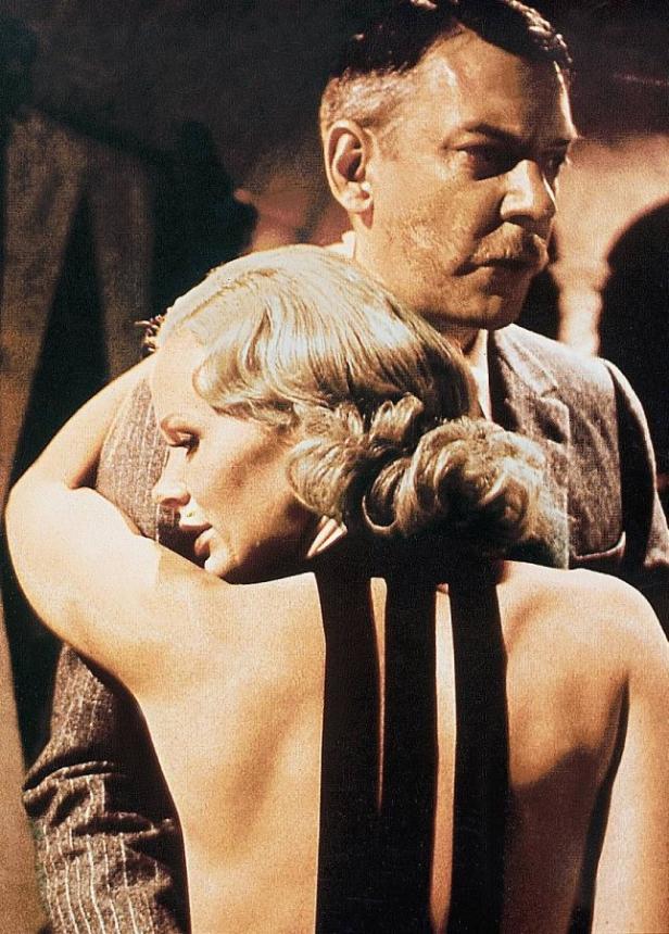 Eine Frau mit freiem Rücken lehnt an einem Mann mit Schnurrbart.