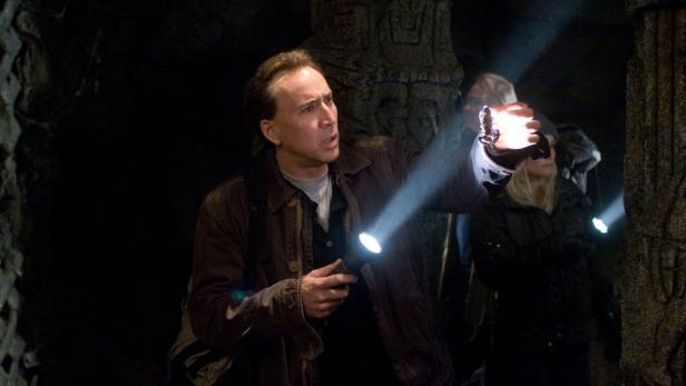 Nicolas Cage leuchtet in einer dunklen Höhle mit einer Taschenlampe.