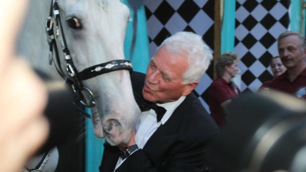 Ein Mann im Smoking gibt einem weißen Pferd einen Kuss.