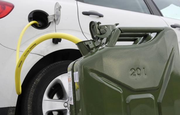 Ein gelber Schlauch führt von einem Benzinkanister in den Tank eines Autos.