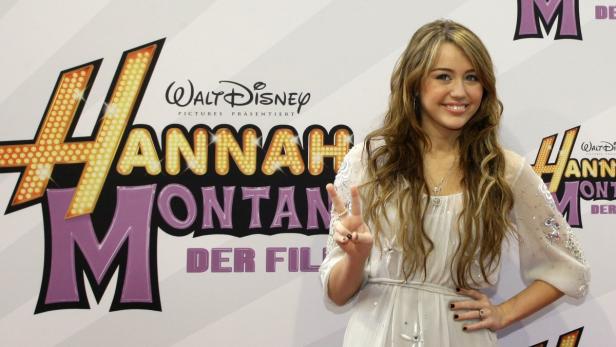 Miley Cyrus posiert vor einem Plakat für „Hannah Montana: Der Film“.