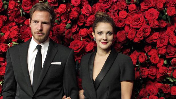 Drew Barrymore und ihr Begleiter posieren vor einer Wand aus roten Rosen.