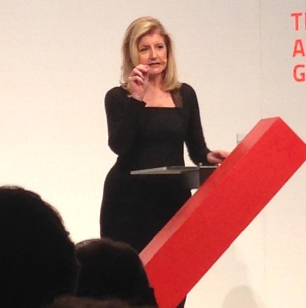 Eine Frau in einem schwarzen Kleid hält eine Rede auf einer Bühne.