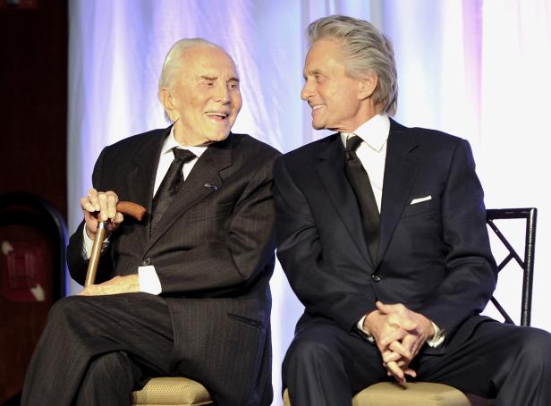 Mike mit Vater Kirk. Kirk und Michael Douglas sitzen nebeneinander und lächeln sich an.