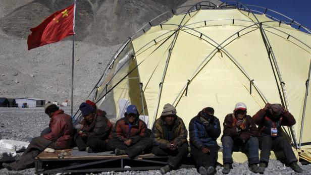 Eine Gruppe von Menschen sitzt vor einem gelben Zelt unter der chinesischen Flagge.