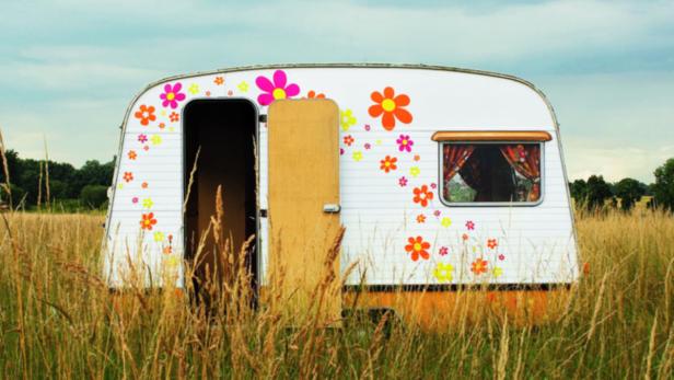 Ein Wohnwagen mit Blumenmuster steht in einem Feld mit hohem Gras.