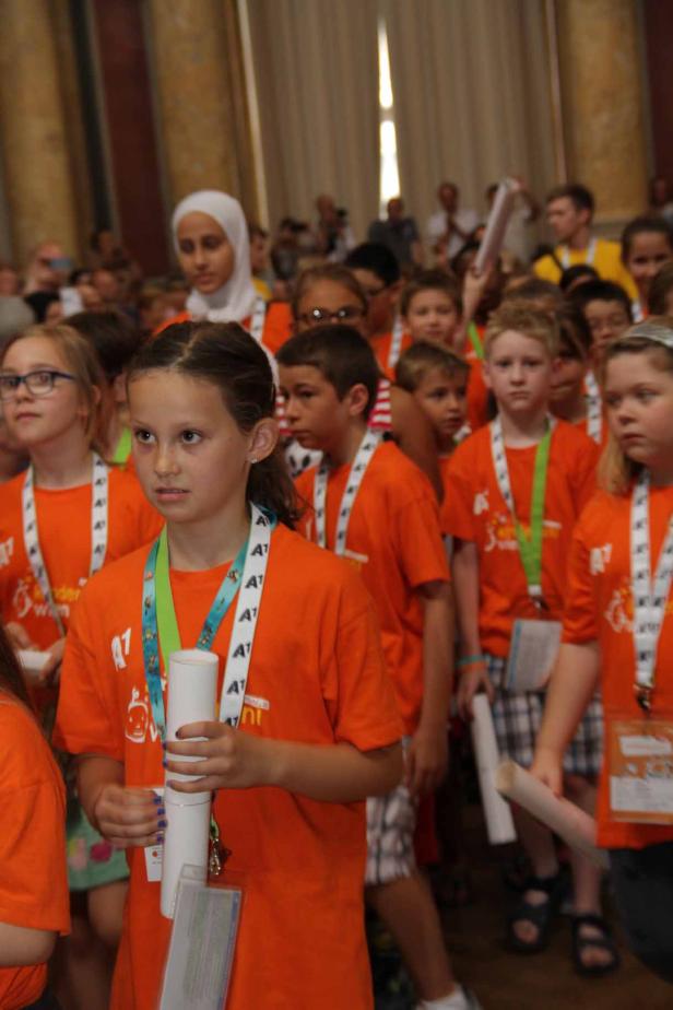 Eine Gruppe Kinder in orangefarbenen T-Shirts steht in einem Raum.