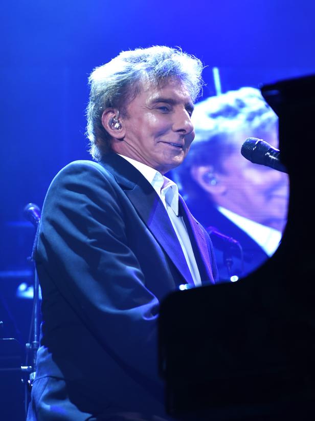 Barry Manilow tritt auf der Bühne vor einem Klavier auf.
