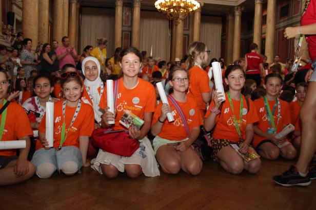 Eine Gruppe von Kindern kniet auf dem Boden und hält Papierrollen in der Hand.