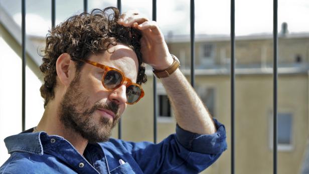 Ein Mann mit Sonnenbrille und lockigem Haar blickt nachdenklich in die Ferne.