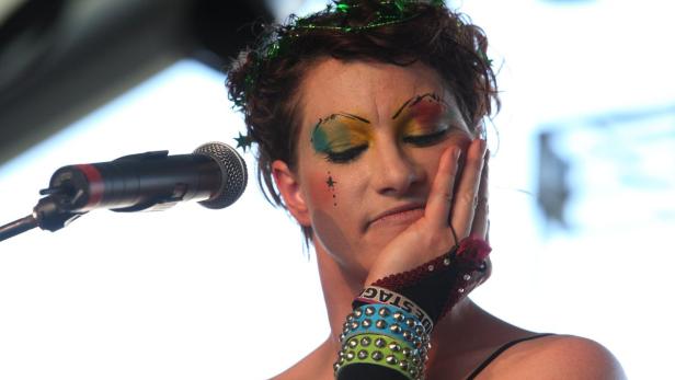 Eine Person mit fantasievollem Make-up steht an einem Mikrofon.