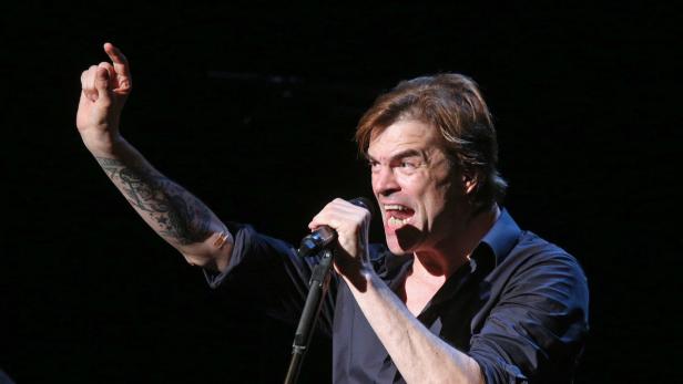 Ein Mann mit Tätowierung singt mit erhobenem Zeigefinger in ein Mikrofon.