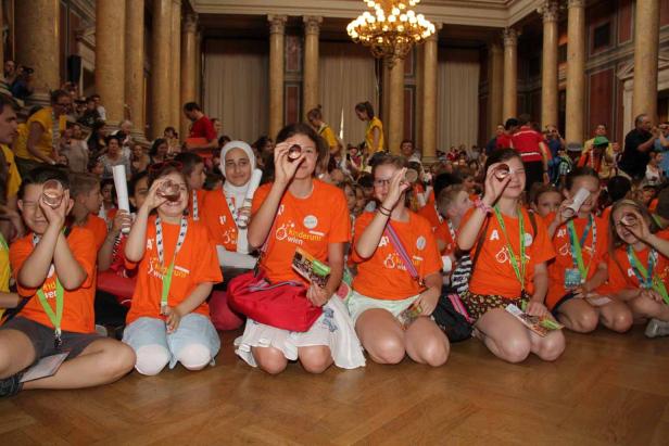 Eine Gruppe Kinder kniet und blickt durch kleine Pappröhren.