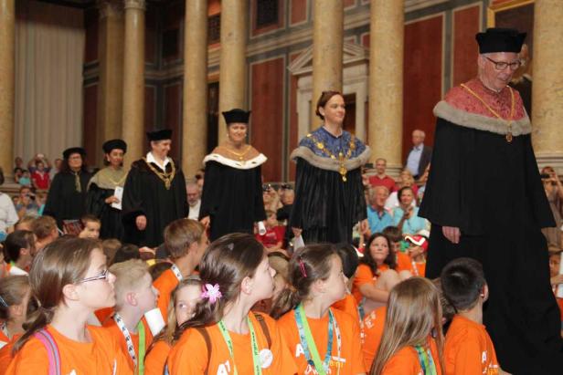 Eine Gruppe von Kindern beobachtet eine Prozession von Würdenträgern in schwarzen Roben.