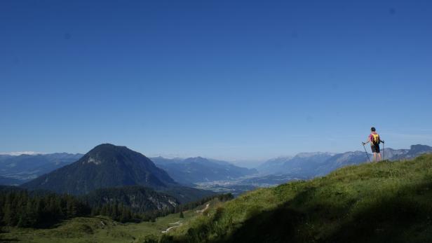 Eine Wanderin genießt die Aussicht auf die Berge und das Tal.