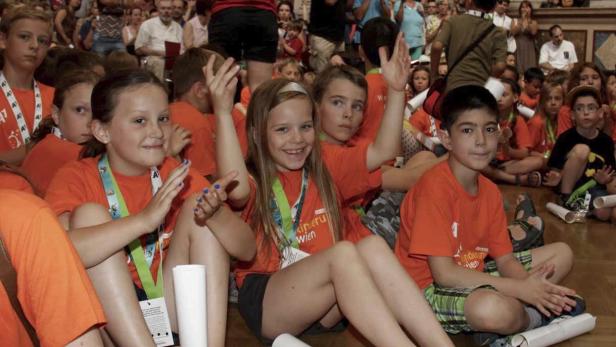 Eine Gruppe Kinder sitzt auf dem Boden und trägt orangefarbene T-Shirts.