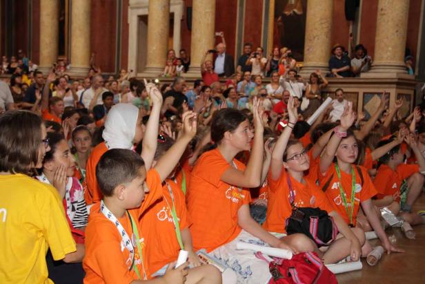 Eine Gruppe Kinder sitzt auf dem Boden und hebt die Hände.