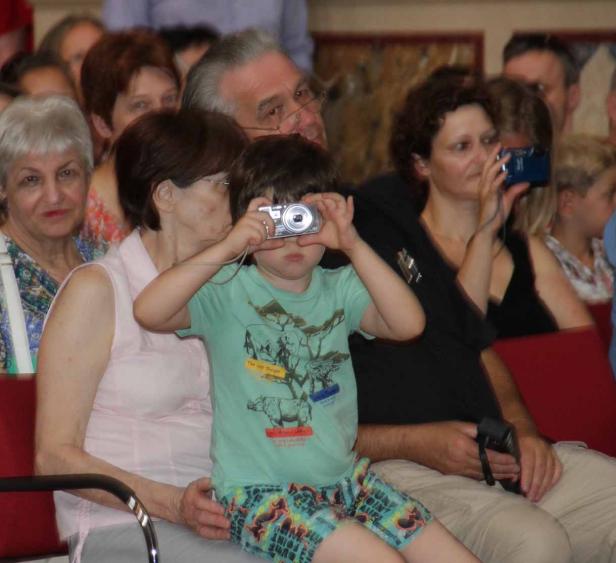 Ein Junge macht mit einer kleinen Kamera ein Foto, während er auf dem Schoß einer Frau sitzt.