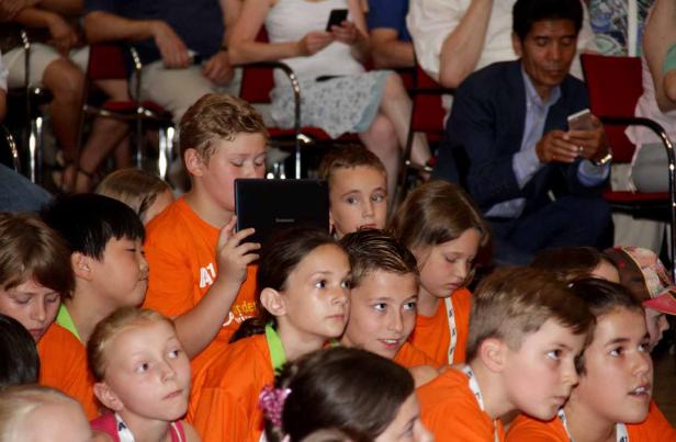 Eine Gruppe von Kindern sitzt in orangefarbenen T-Shirts und schaut aufmerksam zu. Ein Junge hält ein Lenovo-Tablet in der Hand.
