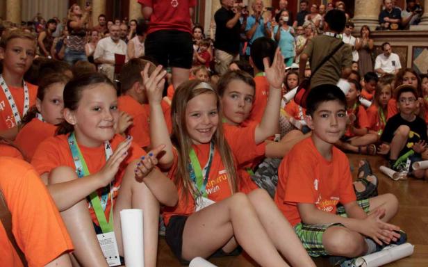 Eine Gruppe Kinder sitzt auf dem Boden und trägt orangefarbene T-Shirts.