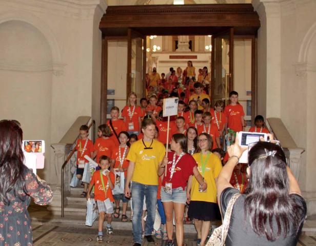 Eine Gruppe Kinder in orangefarbenen T-Shirts verlässt ein Gebäude.
