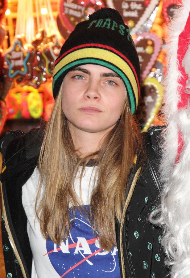 Cara Delevingne mit einer Mütze und einem NASA-T-Shirt vor einem Süßigkeitenstand.