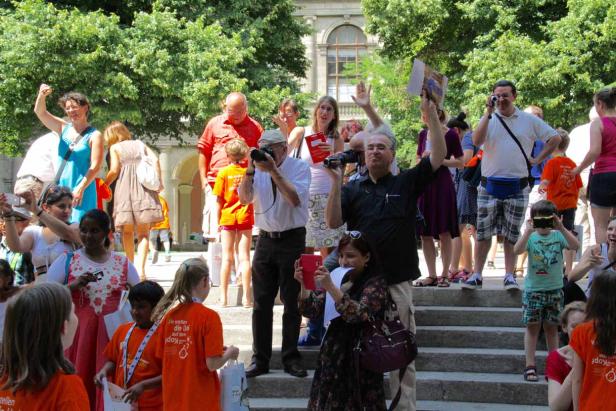 Eine Gruppe von Menschen, viele mit Kameras, versammelt sich im Freien vor einem Gebäude.