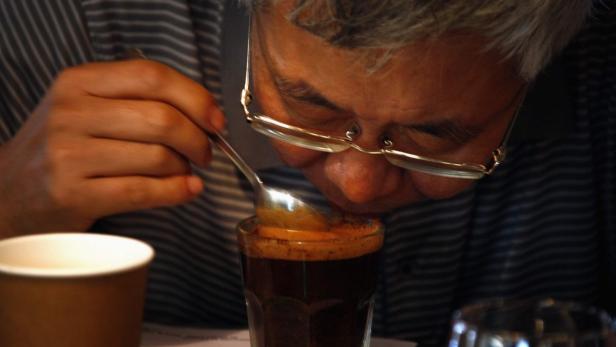 Ein Mann mit Brille probiert mit einem Löffel ein Getränk aus einem Glas.