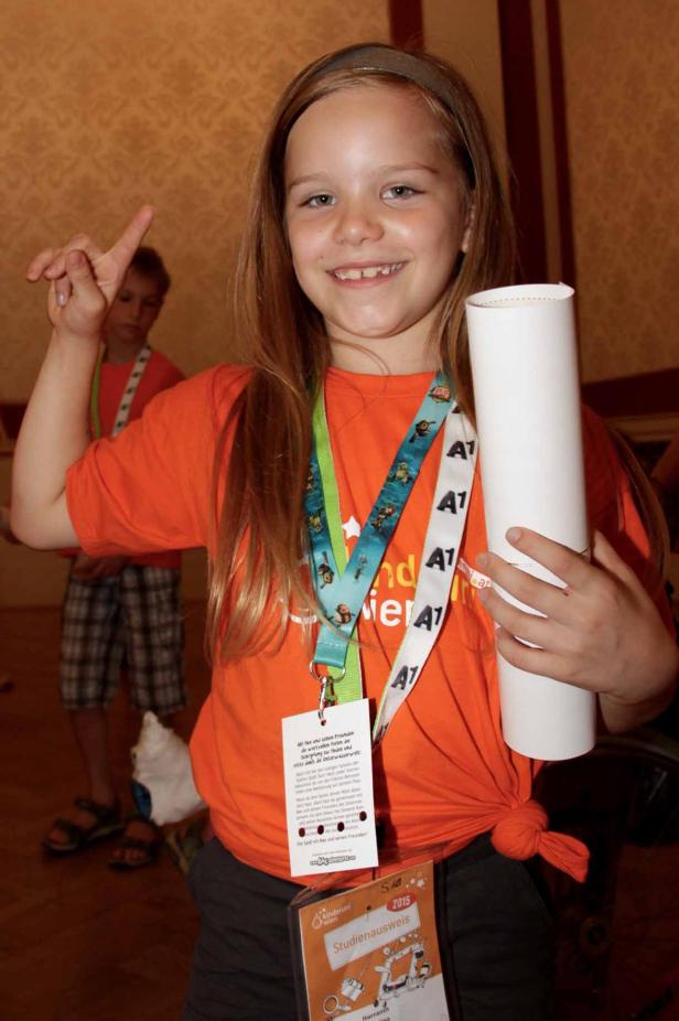 Ein junges Mädchen hält eine Urkunde und zeigt mit dem Finger nach oben.