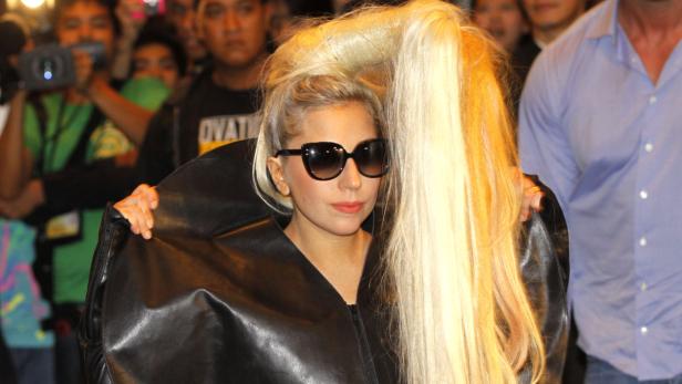 Lady Gaga mit Sonnenbrille und extravagantem blonden Haarteil, umgeben von Menschen.