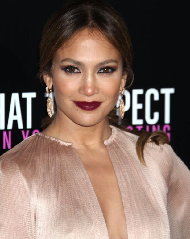 Jennifer Lopez posiert auf einem roten Teppich mit dunklem Lippenstift und Ohrringen.