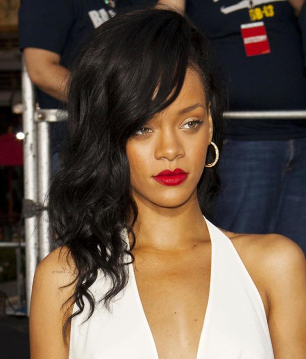 Nahaufnahme von Rihanna mit roten Lippen und gewelltem, dunklem Haar.