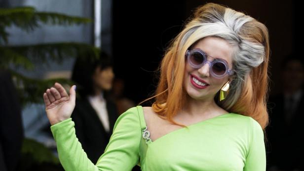 Lady Gaga mit runden Sonnenbrillen und grünem Kleid winkt.