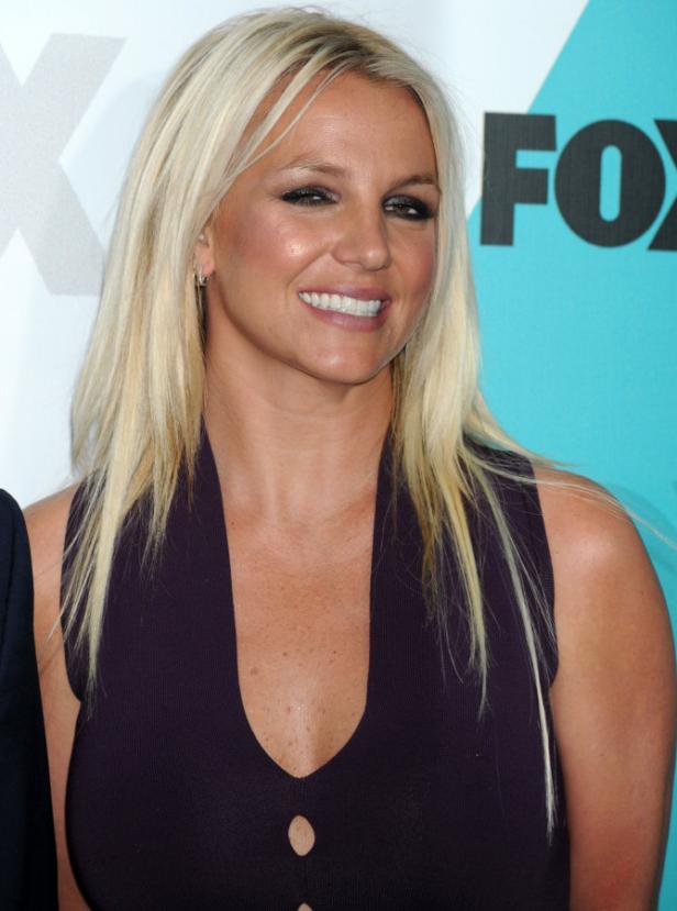 Britney Spears lächelt in einem lila Kleid vor einem FOX-Hintergrund.