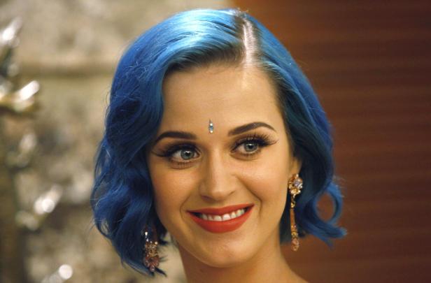 Katy Perry mit blauem Haar, roten Lippen und einem Bindi auf der Stirn lächelt.