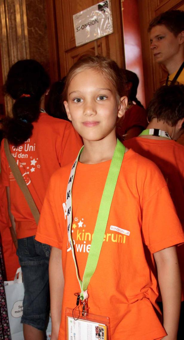 Ein junges Mädchen trägt ein orangefarbenes T-Shirt der Kinderuni.