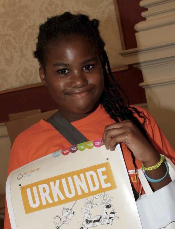 Ein junges Mädchen hält stolz eine Urkunde der Kinderuni Wien in den Händen.