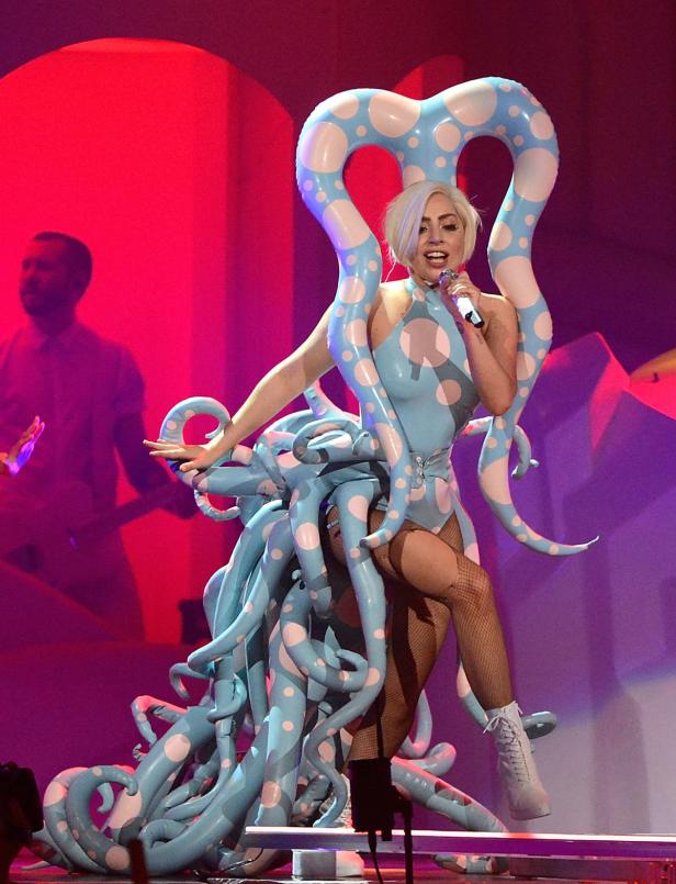 Lady Gaga tritt in einem blauen, gepunkteten Tentakel-Kostüm auf einer Bühne auf.