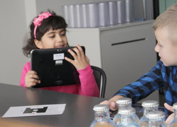 Ein Mädchen mit einem rosa Stirnband benutzt ein Tablet, während ein Junge zusieht.