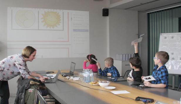 Eine Lehrerin unterrichtet eine Gruppe von Kindern mit einer Projektion von Sonne und Mond im Hintergrund.