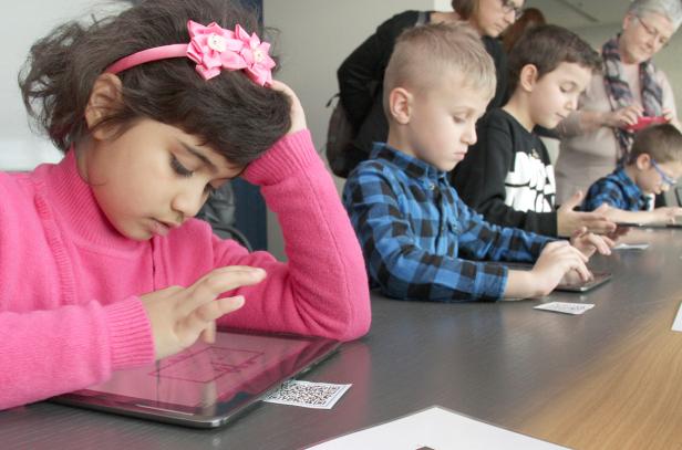 Eine Gruppe Kinder sitzt an einem Tisch und benutzt Tablets.