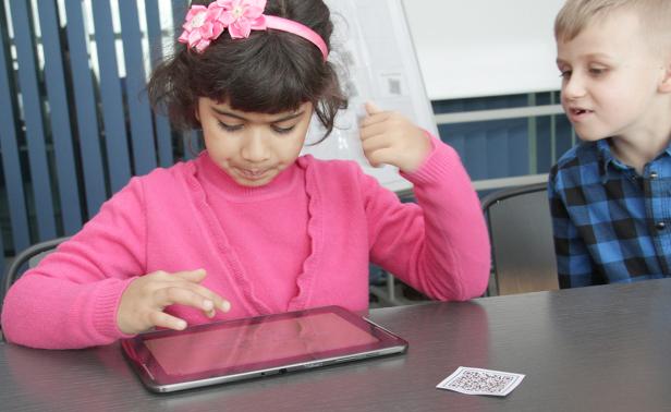 Ein Mädchen mit einem rosa Haarband bedient ein Tablet, während ein Junge zusieht.