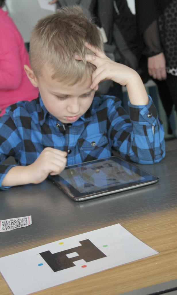 Ein Junge mit blauem Hemd spielt konzentriert auf einem Tablet.