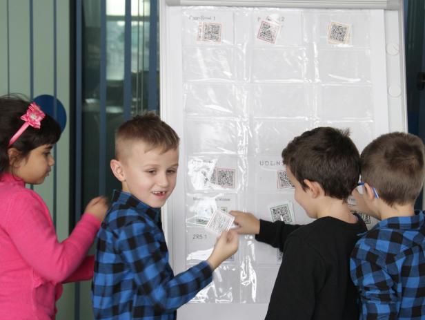 Eine Gruppe Kinder interagiert mit einer Tafel mit QR-Codes in Klarsichthüllen.