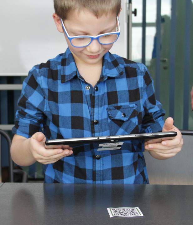 Ein Junge mit Brille scannt einen QR-Code mit einem Tablet.