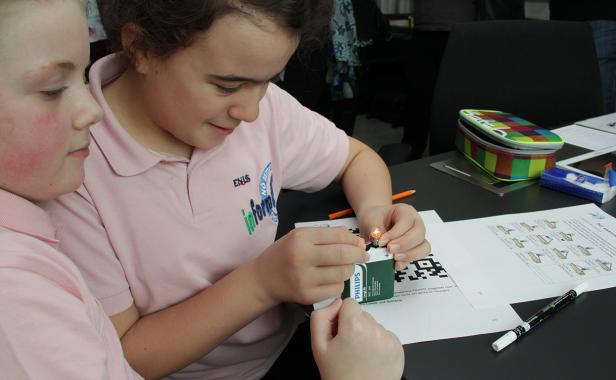 Zwei Mädchen experimentieren mit einer Glühbirne und einer Batterie.