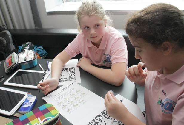 Zwei Mädchen arbeiten an einem Tisch mit Tablets und Arbeitsblättern.