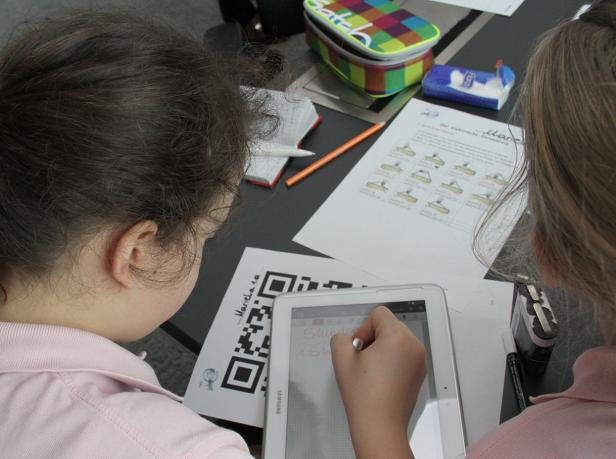 Zwei Mädchen arbeiten an einem Tisch mit einem Tablet und Arbeitsblättern.