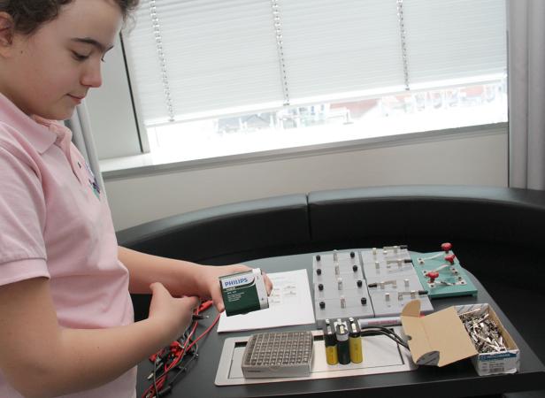 Ein Kind hantiert mit einer Batterie und einem Experimentierkasten.