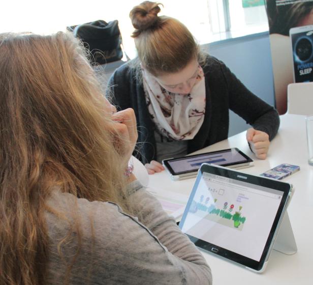 Zwei junge Frauen sitzen an einem Tisch und arbeiten mit Tablets.